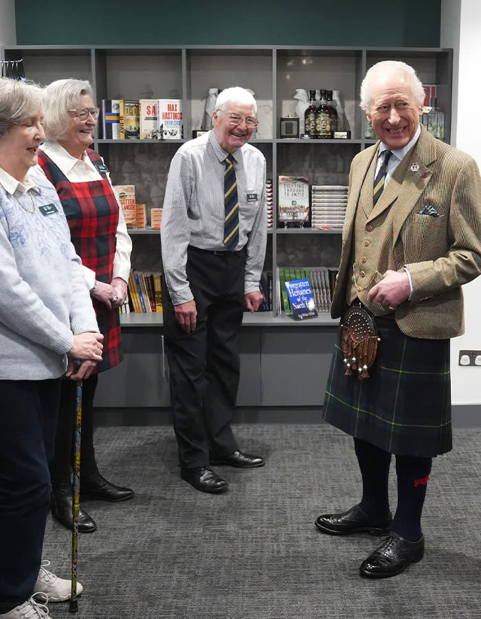 King Charles in a kilt, smiling with three people, sparking concerns over royal crisis.