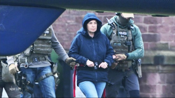 Die mutmaßliche RAF-Terroristin Daniela Klette wird von Polizisten zu einem Hubschrauber geführt. © Screenshot 
