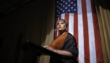 A woman standing at a podium. Behind her is an American flag.