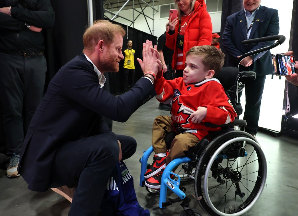 Prince Harry high-fiving a young boy in a wheelchair at the Invictus Games.