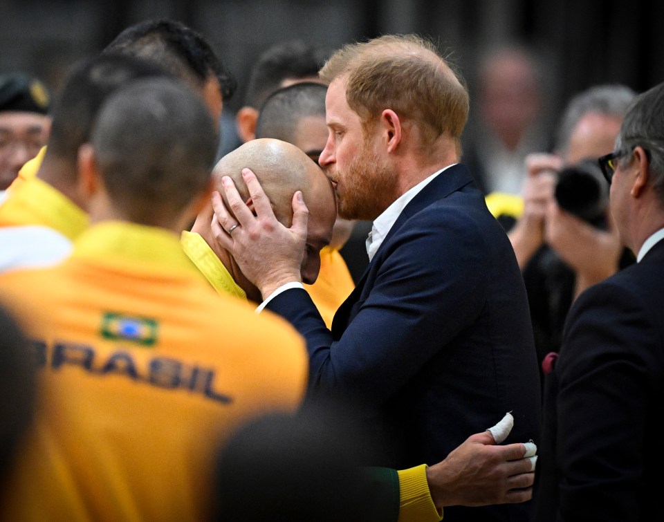 Prince Harry kissing a Brazilian seated volleyball player on the head.