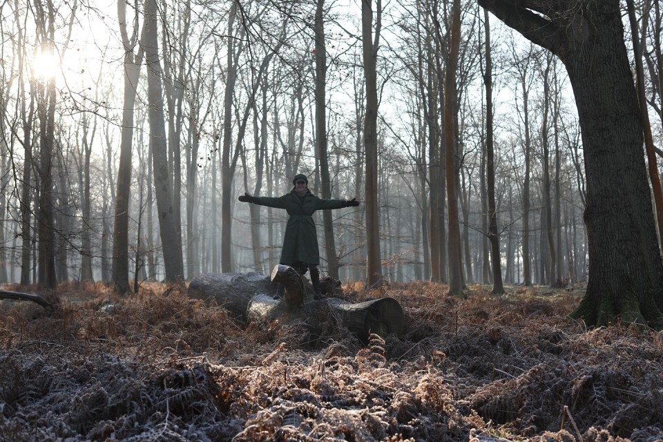 Woman standing on a log in a forest with arms outstretched.