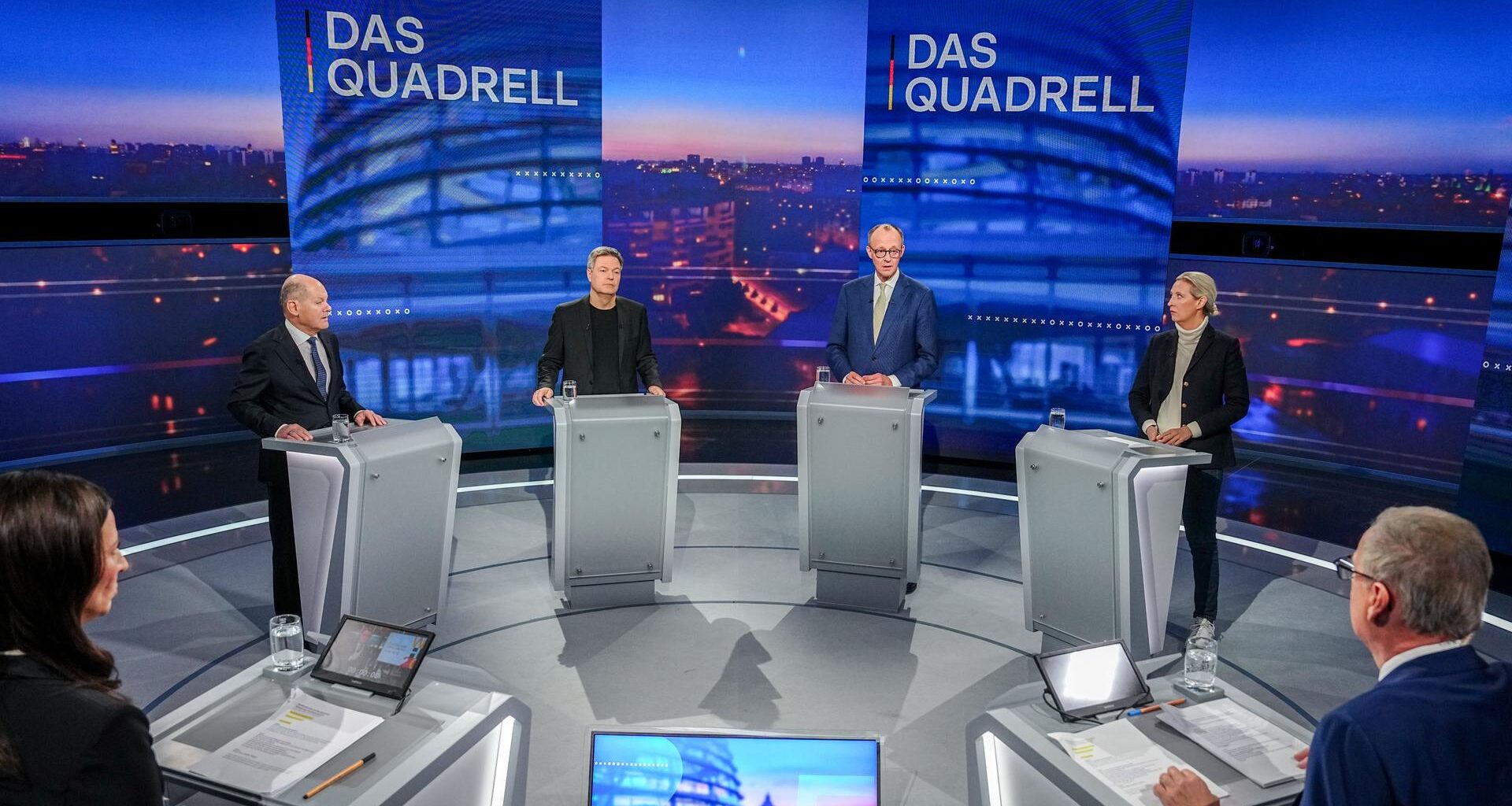Olaf Scholz, Robert Habeck, Friedrich Merz und Alice Weidel stehen an Redepulten auf einer TV-Bühne, im Vordergund zu sehen sind die beiden Moderatoren Pinar Atalay und Günther Jauch.