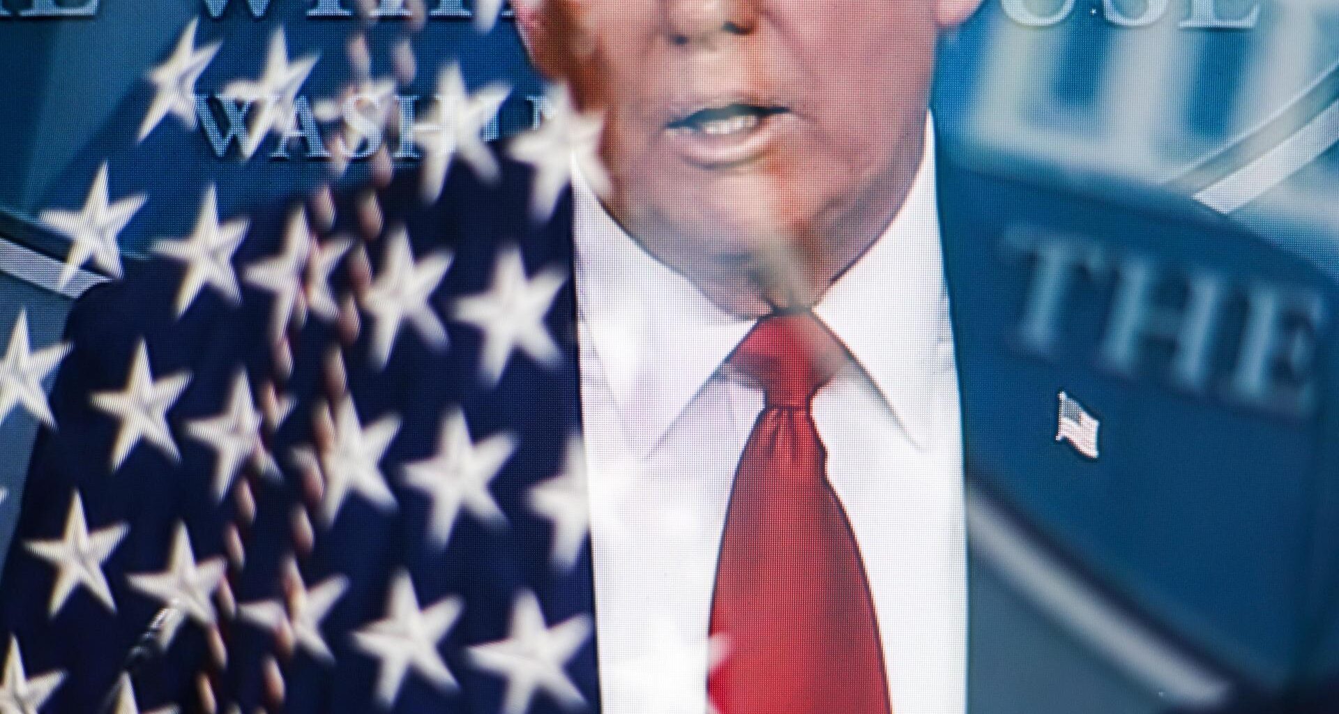 Das durch eine Mehrfachbelichtung in der Kamera entstandene Bild zeigt den Oberkörper Donald Trumps bis zur Nase. Die Augen sind nicht mehr zu sehen. Links neben ihm spiegelt sich eine USA-Flagge.