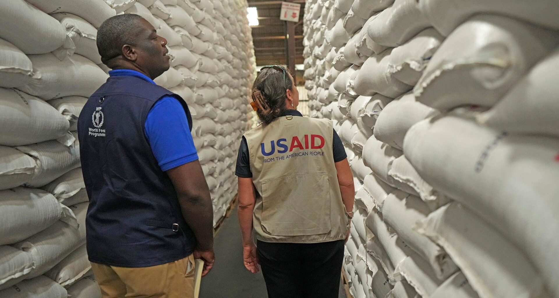 Ein Mitarbeiter des Welternährungsprogramms und eine Mitarbeiterin von USAID inspizieren Getreidesäcke in einer Lagerhalle.