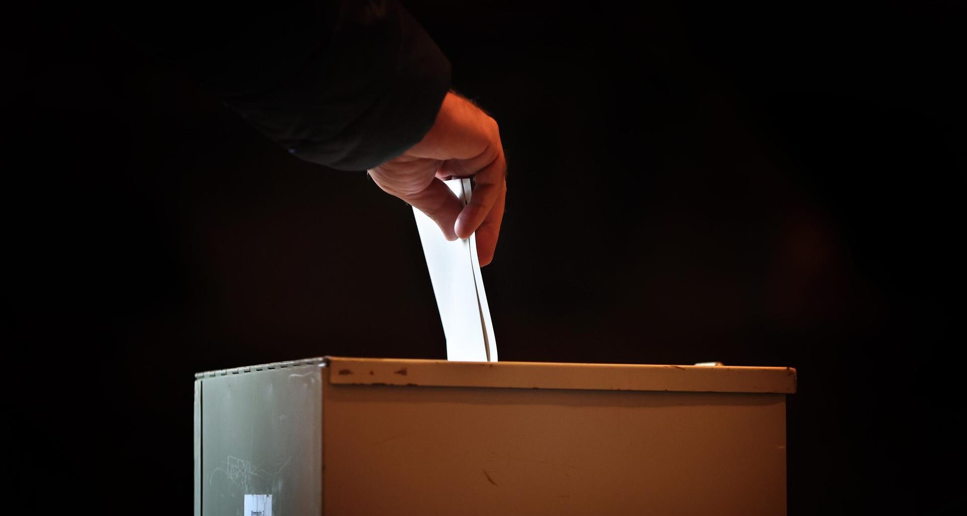 Ein Wähler steckt in einem Wahllokal seinen Stimmzettel in eine Wahlurne.