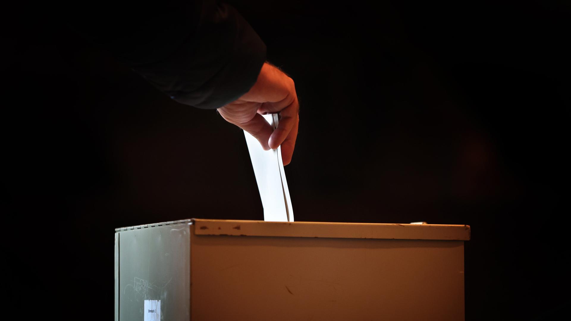 Ein Wähler steckt in einem Wahllokal seinen Stimmzettel in eine Wahlurne. Ein Wähler steckt in einem Wahllokal seinen Stimmzettel in eine Wahlurne.