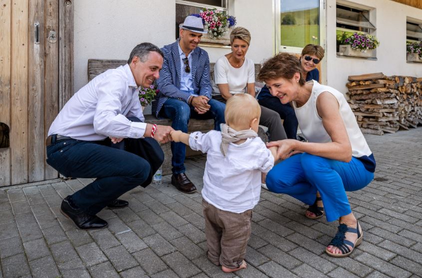 Five adults greet a small child