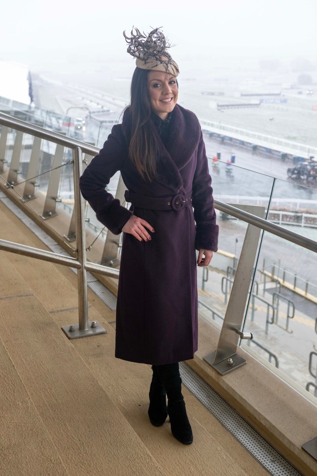 A woman in a purple coat and hat stands on a balcony overlooking a race track.