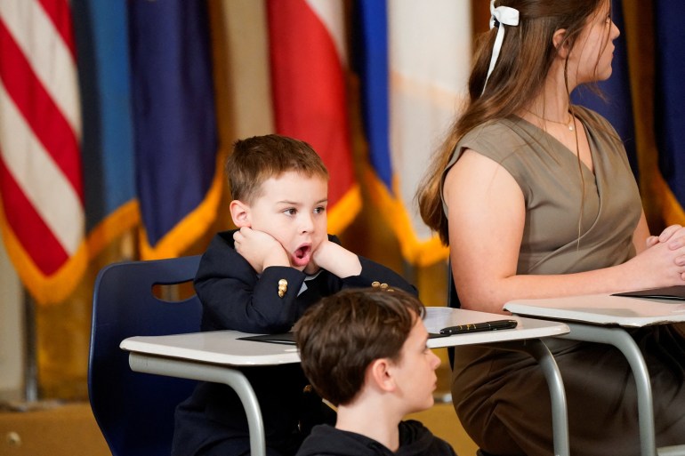 A kid behind a desk at the East Room event opens his mouth and puts his hands on his face, in seeming shock — or maybe a yawn