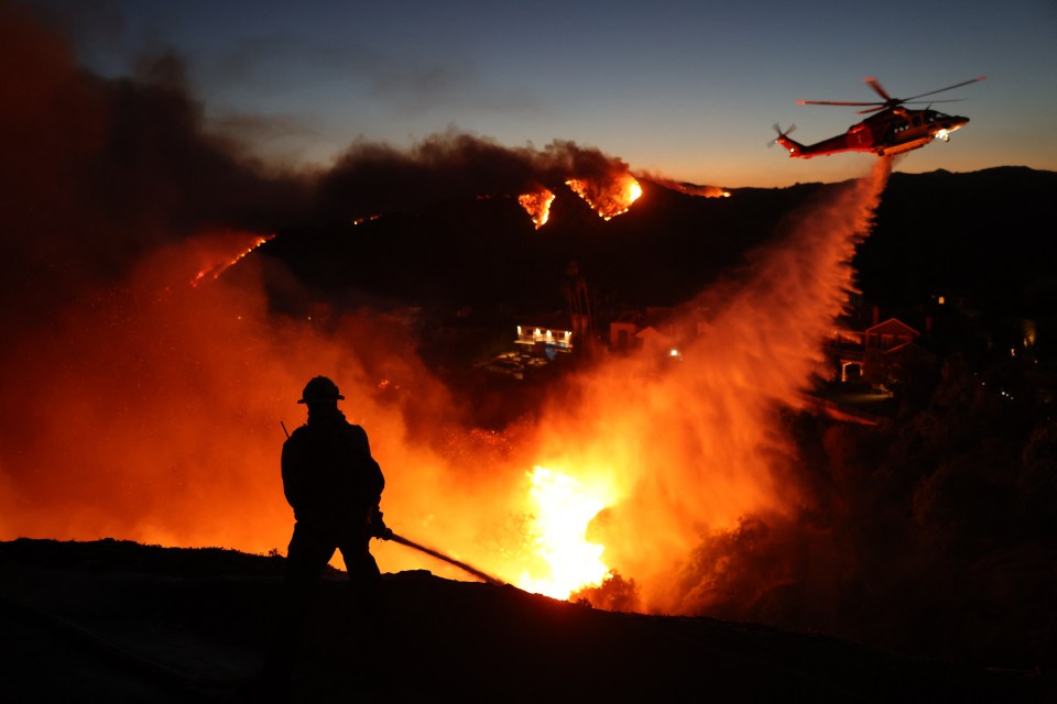 Firefighter battling wildfire at night; helicopter dropping water.