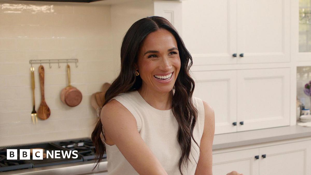 A photograph of Meghan, Duchess of Sussex, smiling while wearing a sleeveless white jumper
