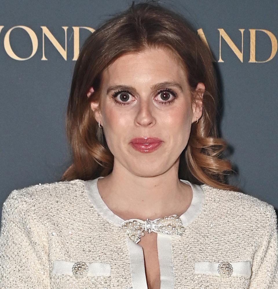Princess Beatrice wearing a white dress with a cutout featuring bows standing in front of a gray backdrop.