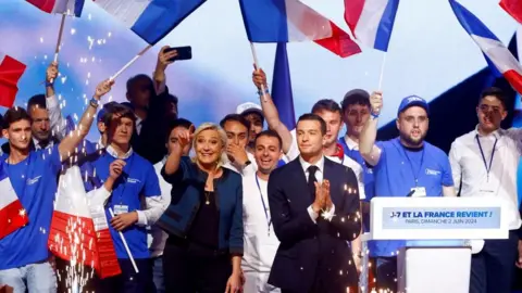 Reuters A woman and a man stand on a stage surrounded by supporters and French flags.