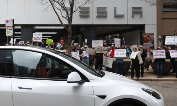A motorist drives a Tesla past a Tesla dealership at 901 N. Rush St. as people gesture at the driver while protesting Tesla chief executive Elon Musk's involvement in federal government affairs during a demonstration called, "Tesla Takedown" Saturday, March 29, 2025, in Chicago. (John J. Kim/Chicago Tribune)