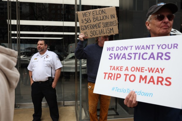 A police supervisor guards an entrance to a Tesla dealership at 901 N. Rush St. as people hold signs to protest Tesla chief executive Elon Musk's involvement in federal government affairs during a demonstration called, "Tesla Takedown" Saturday, March 29, 2025, in Chicago. (John J. Kim/Chicago Tribune)