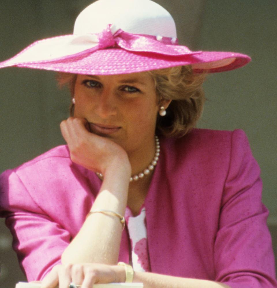 Princess Diana wearing a pink blazer and white hat resting her chin on her hand at the 1987 Epsom Derby .