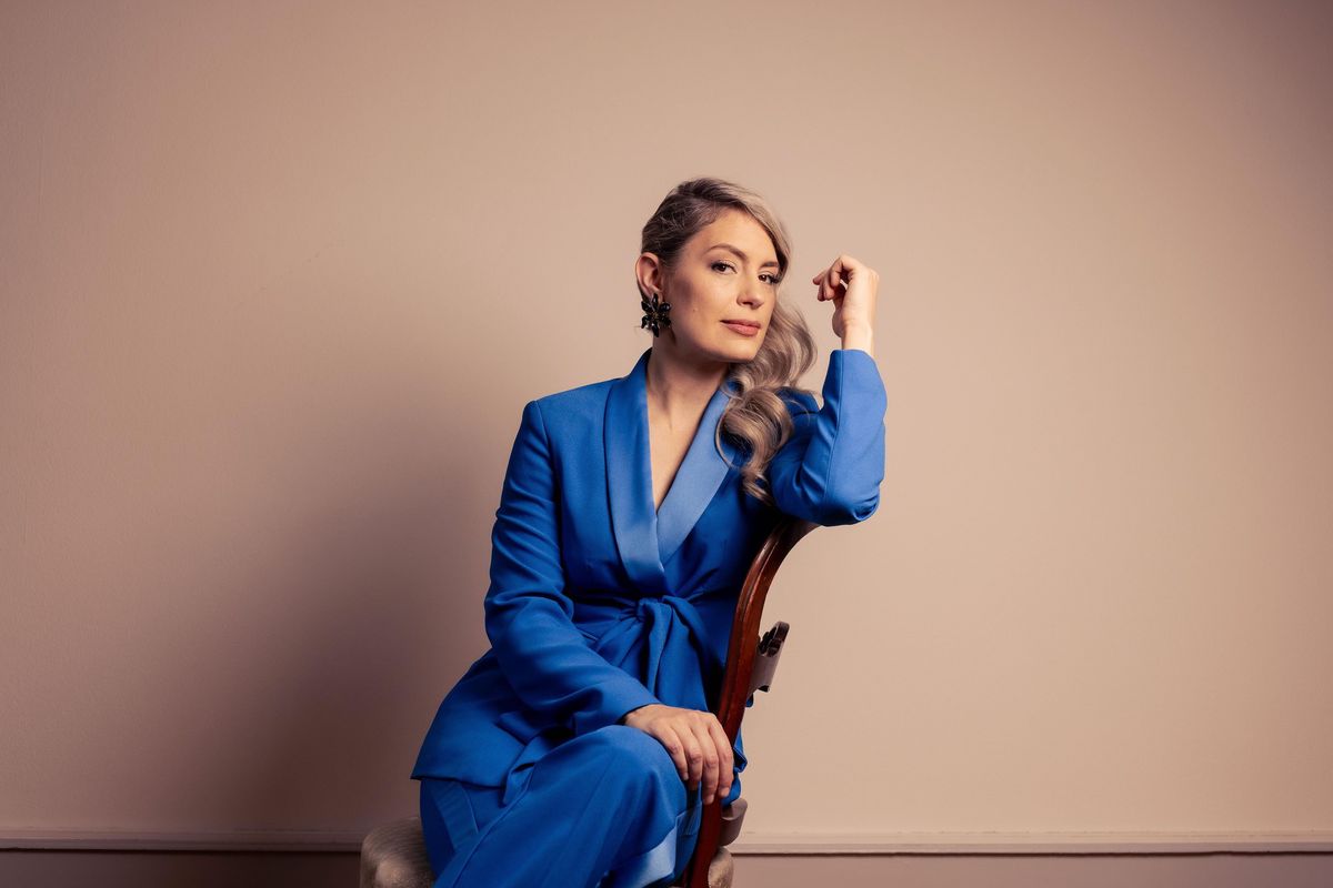 Femme en costume bleu posée de manière élégante sur une chaise.
