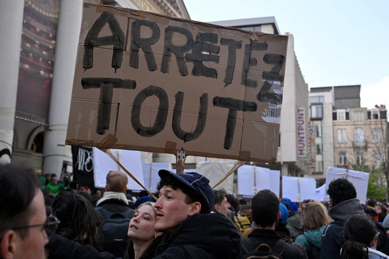 Photo shows large crowd of protesters and a placard reading "Stop everything" in French