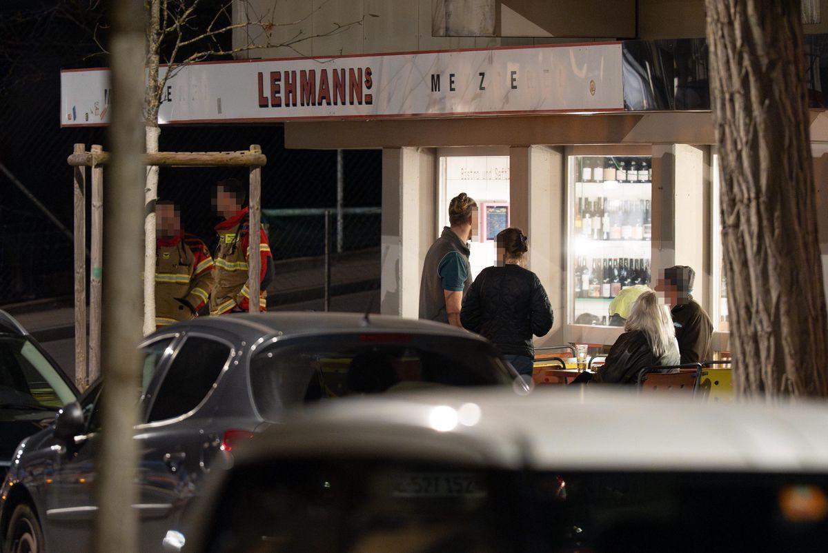 Menschen stehen nachts vor einem Imbiss namens ’Lehmann’. Im Vordergrund sind parkende Autos sichtbar.