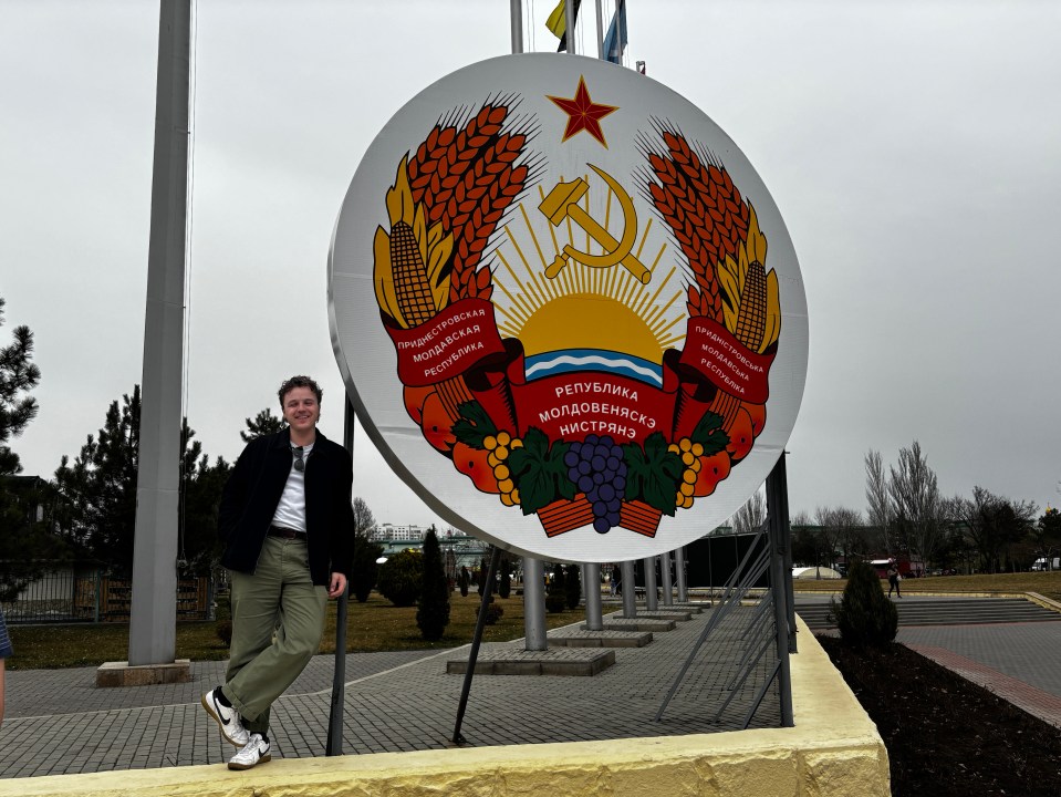 Person standing near large Transnistria coat of arms.