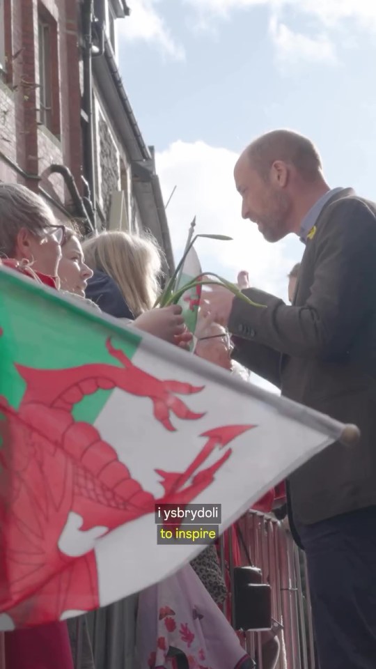 Man receiving flowers from children holding Welsh flag.