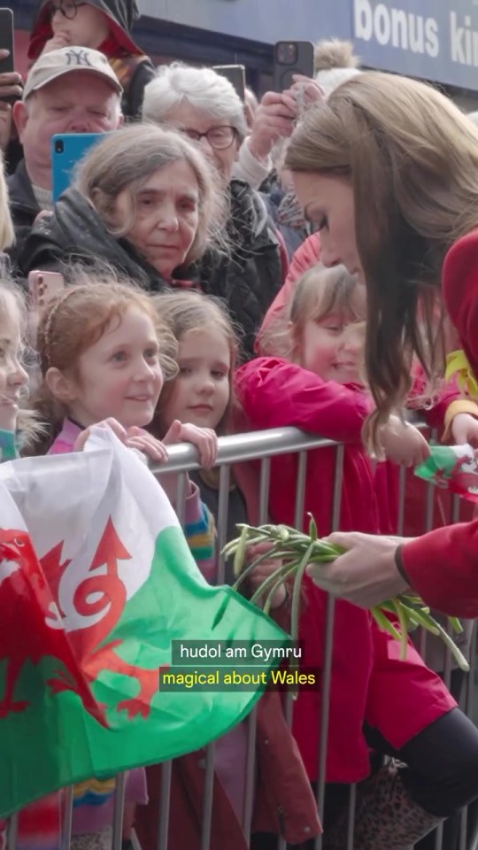 Kate Middleton receiving flowers from children behind a barrier.