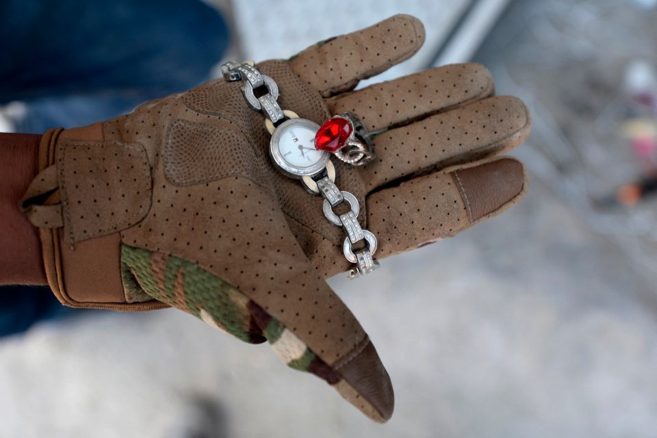 A gloved hand holding a watch and ring found at a crime scene.