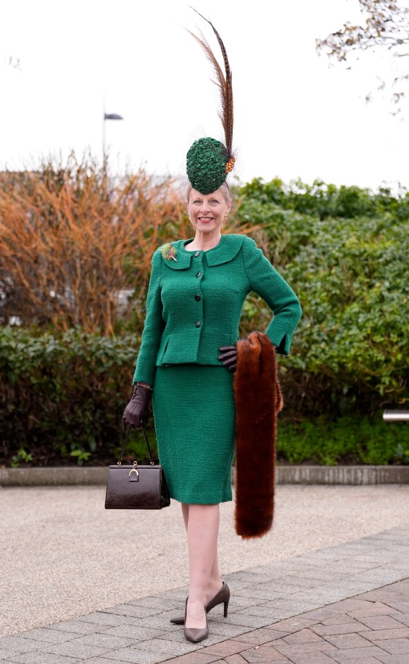 Woman in green suit and hat at a racecourse.