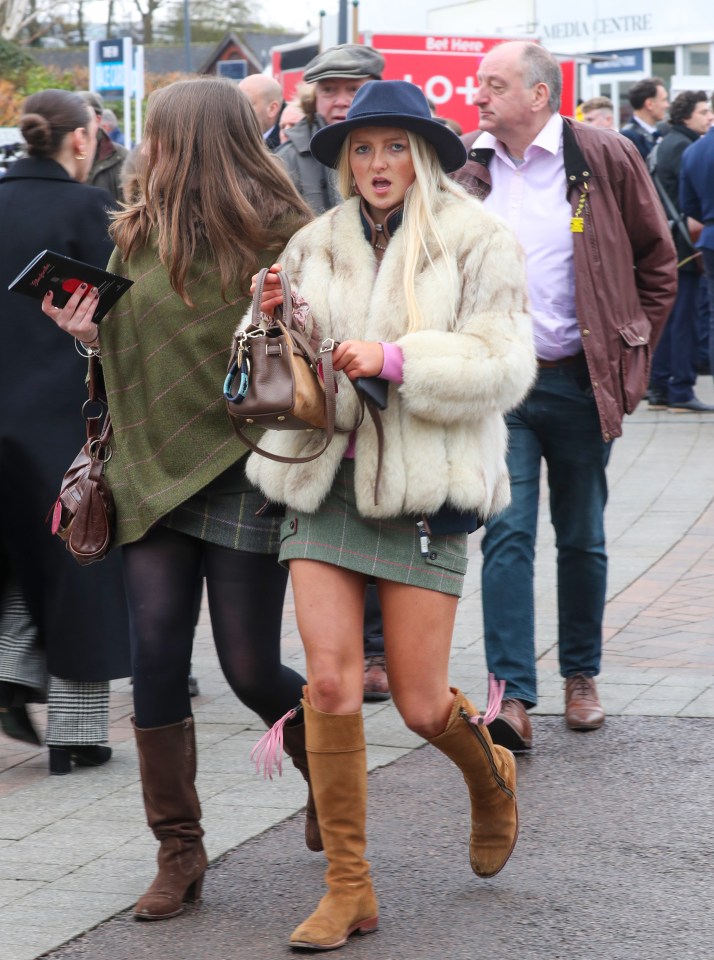 Woman in a fur coat and knee-high boots at a horse racing festival.