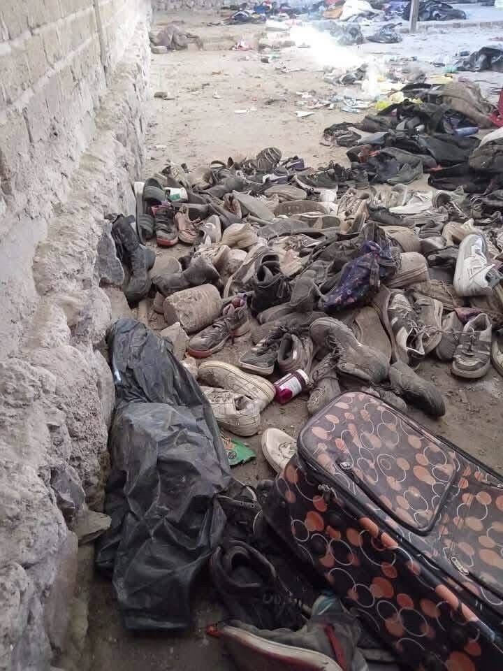 Pile of shoes and a suitcase near a wall.