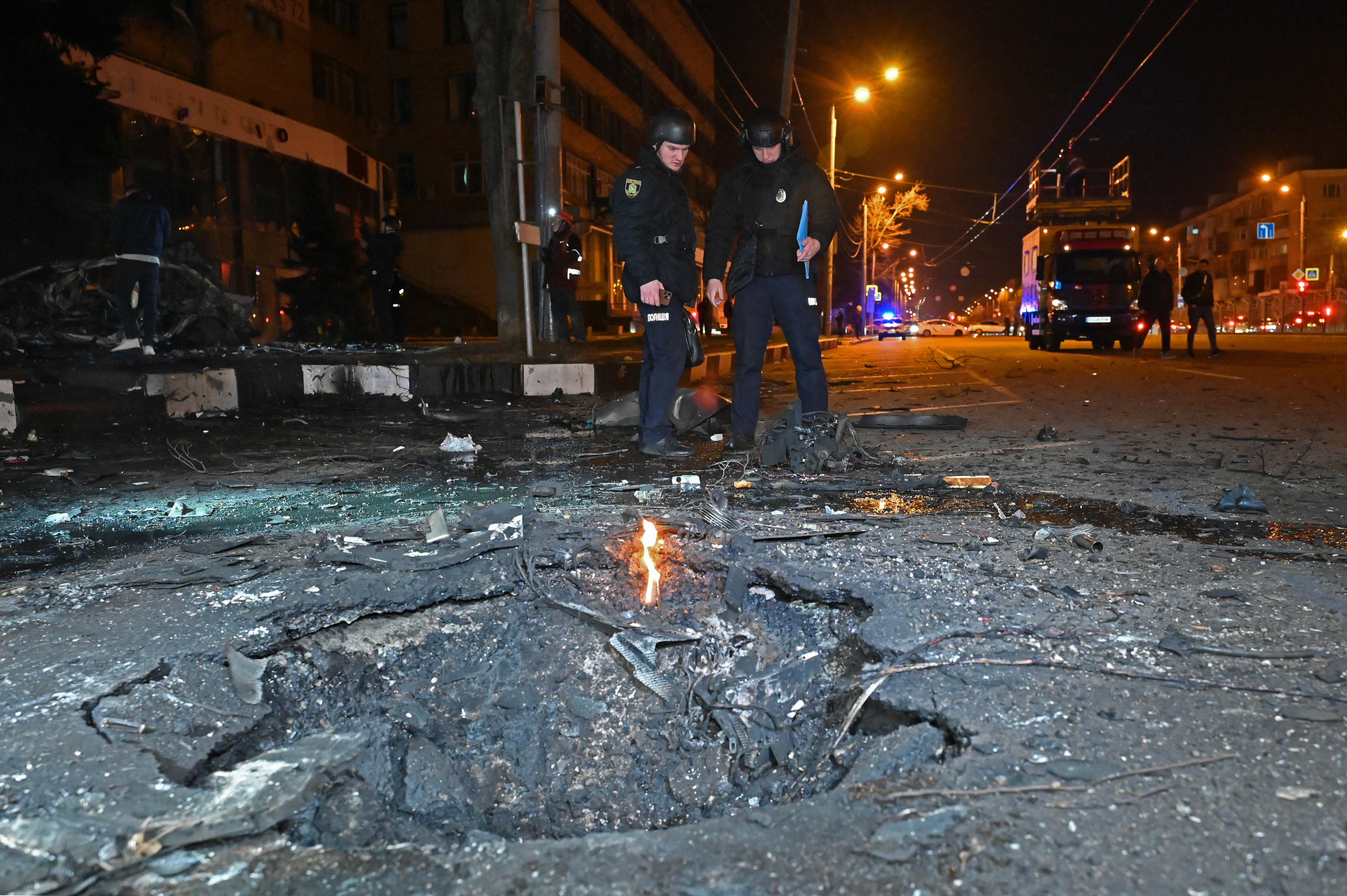 Police officers stand near a crater after the explosion