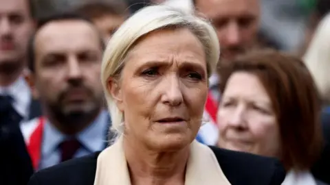 Reuters A woman with blonde hair wearing a black and white jacket looks cautious at a rally surrounded by other people.