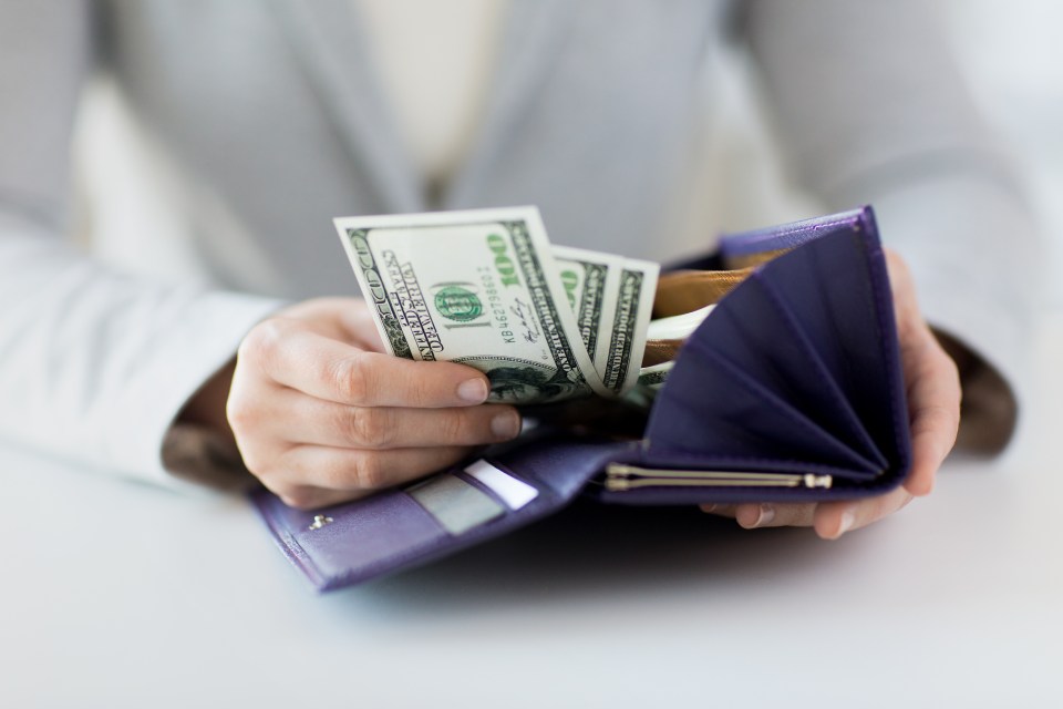 Woman's hands holding a purple wallet with US dollar bills.