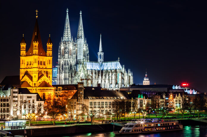 Cologne Cathedral and Great St. Martin Church illuminated at night, symbolizing Germany’s growth.