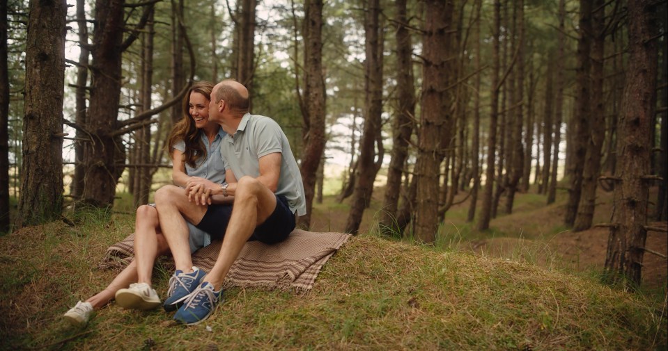 a man and woman sit on a blanket in the woods