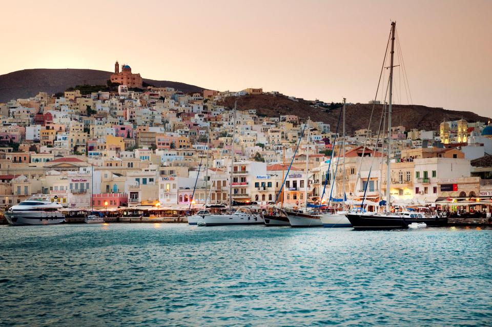 Syros harbor at dusk, with sailboats and a hillside town.