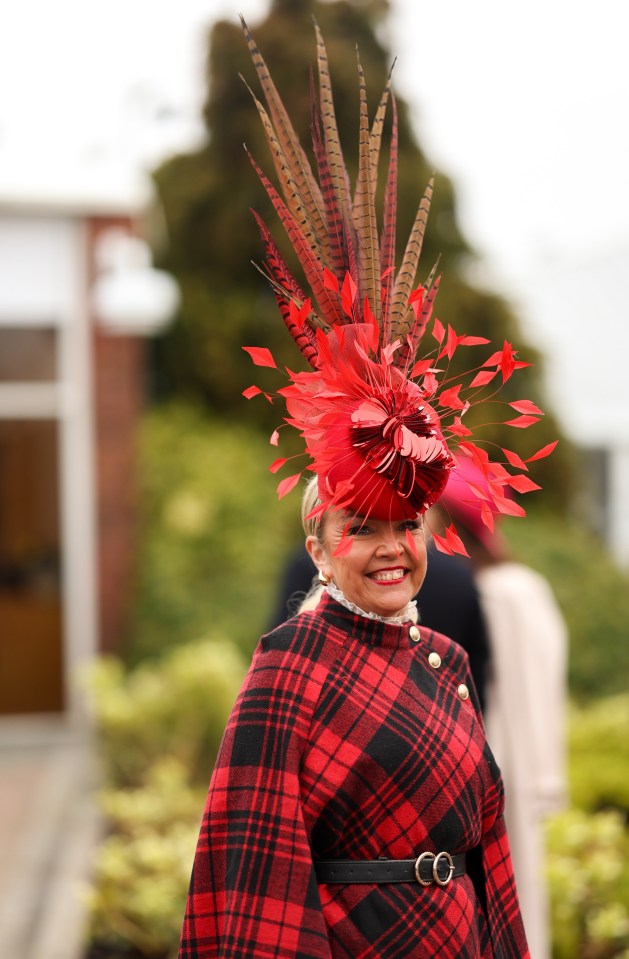 Woman in red plaid coat and large red hat with feathers at a horse race.