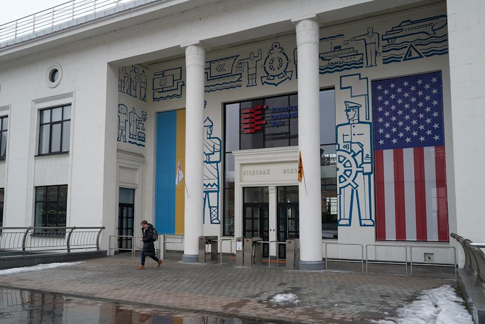 A white building has American and Ukraine flags draped on either side of an entrance.