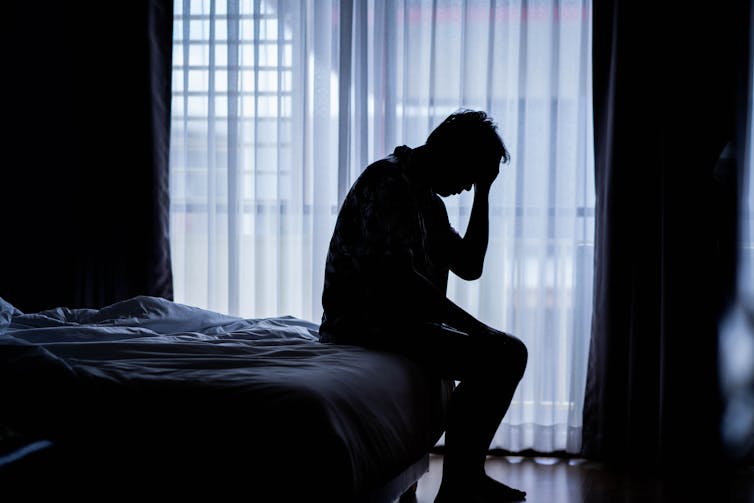 Lonely man silhouette sitting on the bed feeling depressed and stressed in the dark bedroom