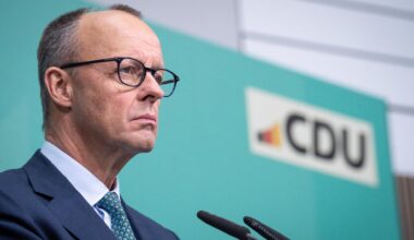 Merz steht bei einer Pressekonferenz mit ernstem Blick am Mikrofon vor einem türkisen Hintergrund mit dem Logo der CDU.
