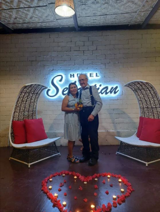 Couple posing in front of Hotel Sebastian sign with heart-shaped candle and flower arrangement.