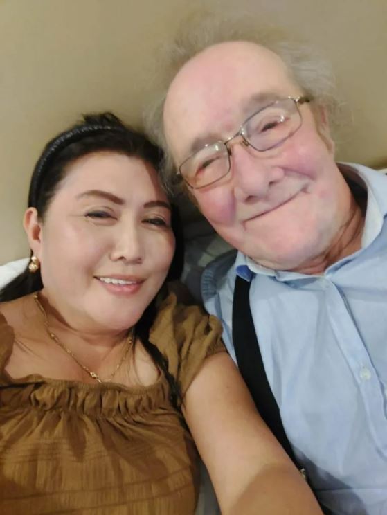 Photo of an older man and a younger woman posing closely together.