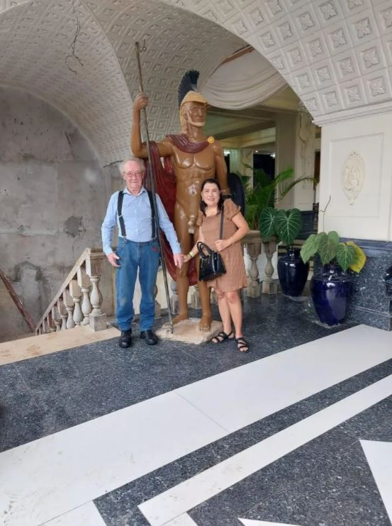 Elderly couple posing with a statue of a male warrior.