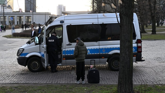 A man with luggage waits next to a police van as a Polish police officer checks his documents in Warsaw