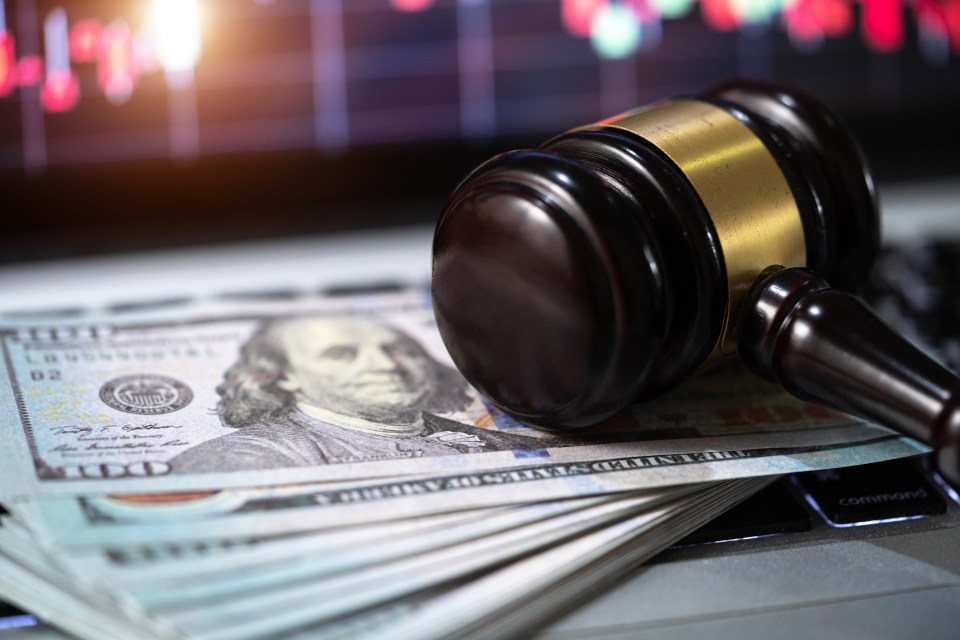 Gavel on a stack of US currency on a laptop with a stock market graph in the background.