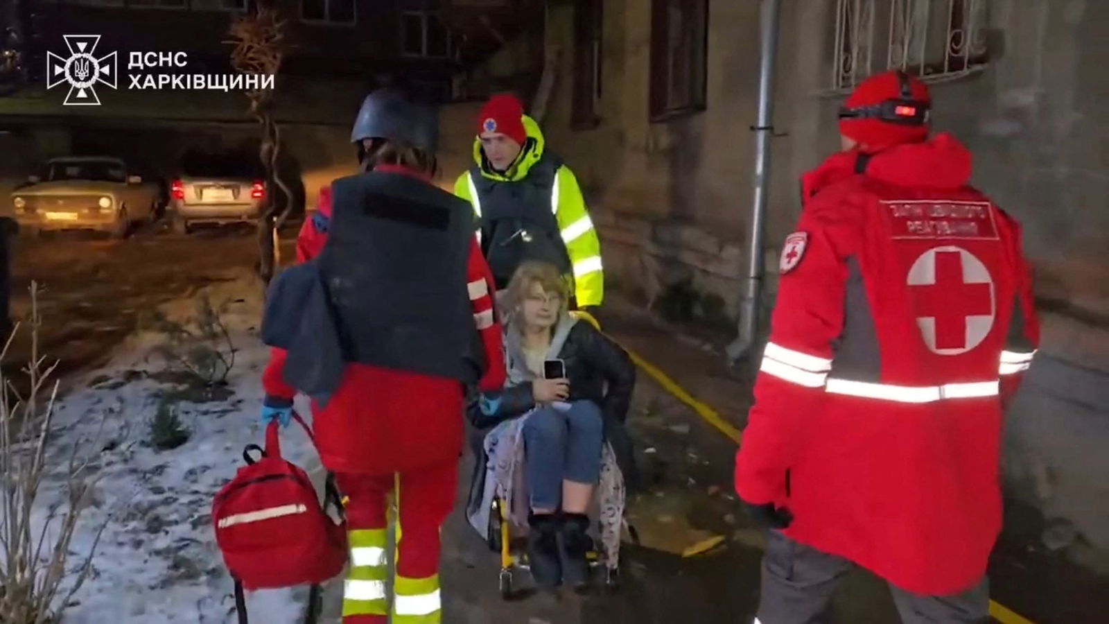 Emergency workers help a woman in a wheel chair. 