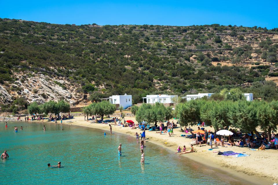 Beach scene at Faros, Sifnos, Greece, with people swimming and relaxing on the sand.