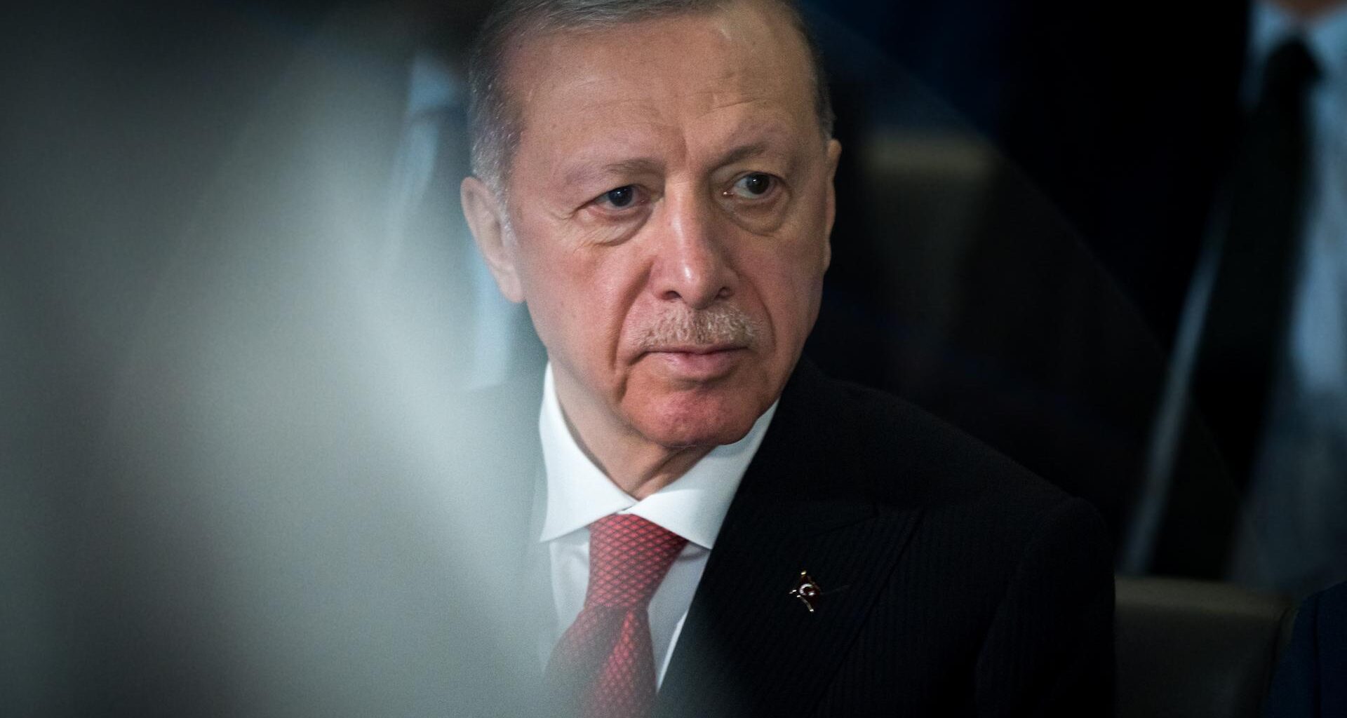 Porträt von Recep Tayyip Erdogan, der ein weißes Hemd, eine rote Krawatte und ein schwarzes Sakko trägt und an der Kamera vorbeischaut.