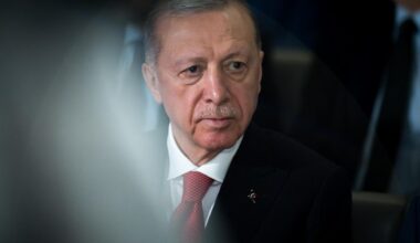 Porträt von Recep Tayyip Erdogan, der ein weißes Hemd, eine rote Krawatte und ein schwarzes Sakko trägt und an der Kamera vorbeischaut.